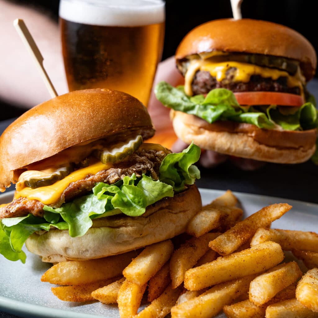 Two burgers being held over a plate of chips